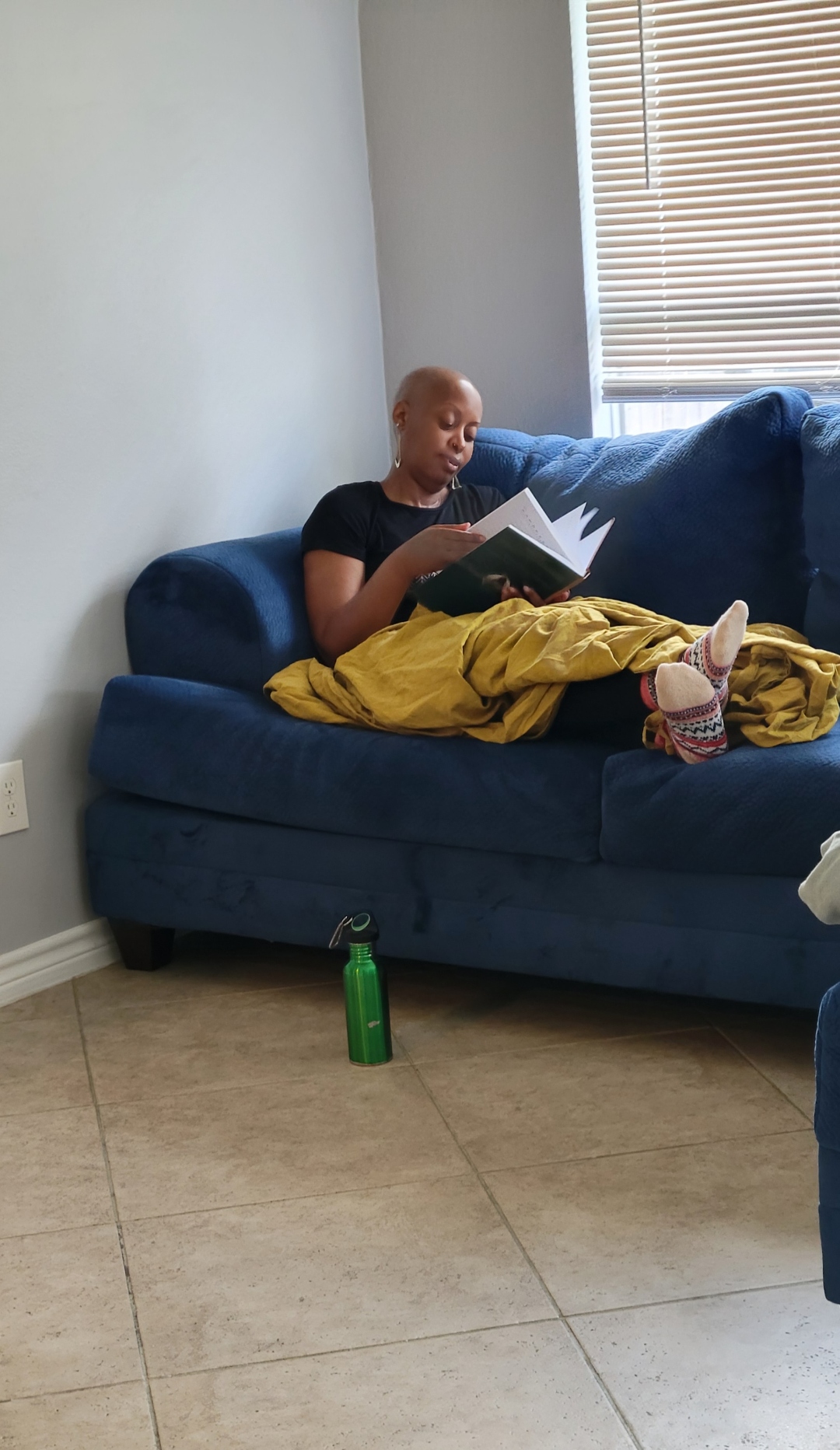 A woman wrapped in a yellow blanket resting with the We Rest as Reparations journal